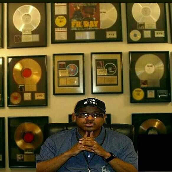 Celebrity DJ Cat-X seated in front of a wall of RIAA Gold and Platinum certified record plaques from his major label promo career